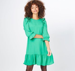 A woman wearing a green ruffle sleeve tiered dress with black tights.