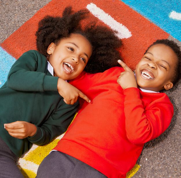 Two children laughing on a playground in school uniforms.