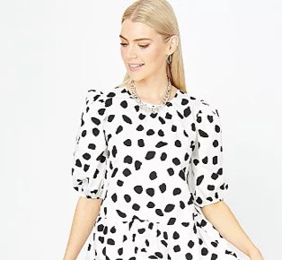 Woman poses looking to one side wearing white abstract spot print tiered poplin dress, silver-tone earrings and silver-tone chain necklace.