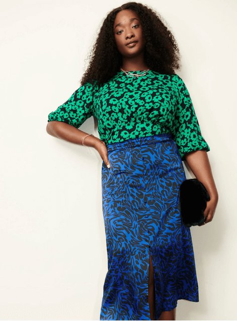 A woman wearing a green floral top with a blue patterned skirt