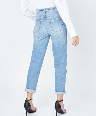 A reverse shot of legs of a woman wearing white long sleeve top, light wash blue jeans and black heeled sandals.