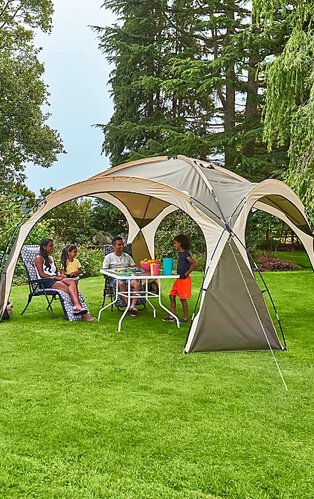 Cream ozark camping sun shelter with family surrounding a table in a field.