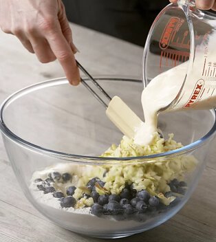 Hands pouring liquid from Pyrex jug into glass bowl containing food.