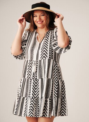 A woman posing in a monochrome print dress and black sunhat.