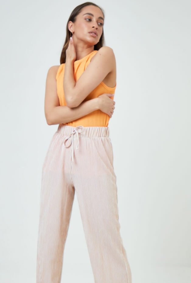 A woman posing in an orange top and cream trousers.