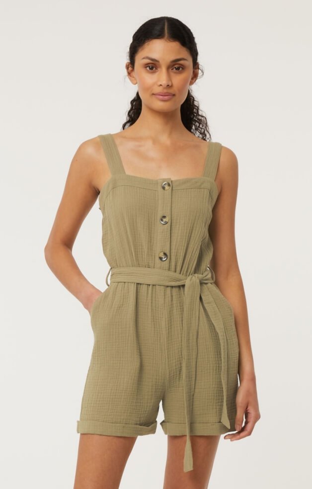A woman wearing a khaki playsuit with one hand in her pocket.