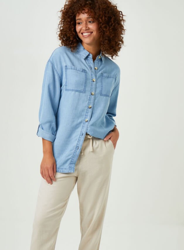 A woman posing in cream trousers and a light blue shirt.