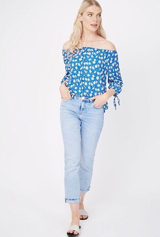 Woman wearing a blue off the shoulder top with light wash straight cut jeans and sliders