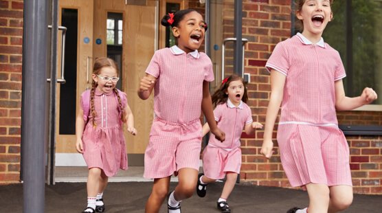 Four girls wearing red gingham dresses smiling and running out of school