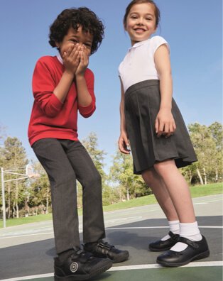 A boy wearing grey trousers, a white polo and a red jumper, standing outside next to a girl wearing a white polo and a grey skirt