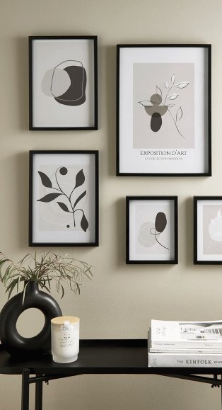 A black consol table with decor items in front of a wall with a selection of black frames.