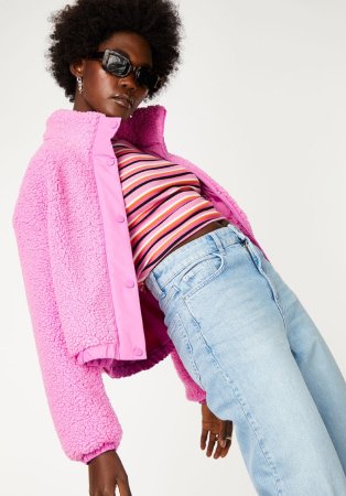Woman wearing pink cropped fluffy jacket, striped shirt, light blue jeans.
