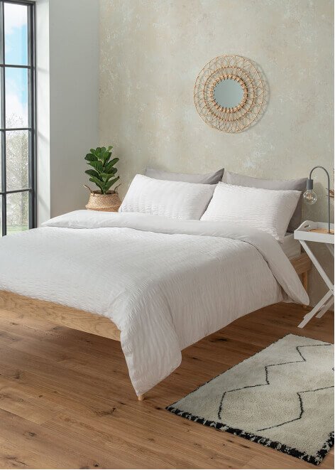 A bedroom with a double bed, white seersucker duvet set, wall mirror and decorative plants