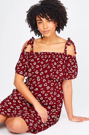 Woman poses sitting on floor wearing maternity leopard print cold shoulder nursing midi dress.