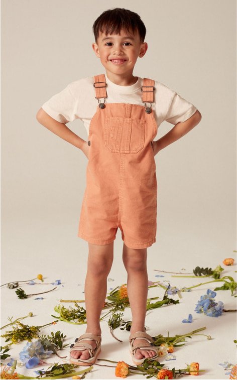 A child wearing orange dungaree shorts and white t-shirt.