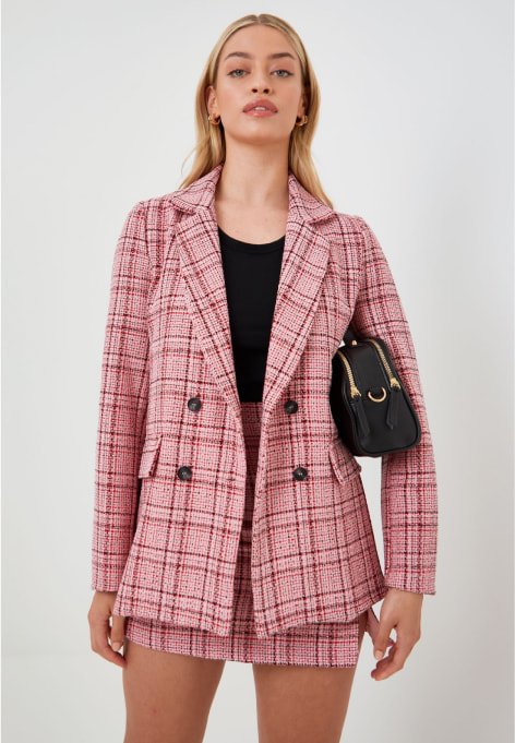 A woman wearing a pink boucle checked blazer and skirt.