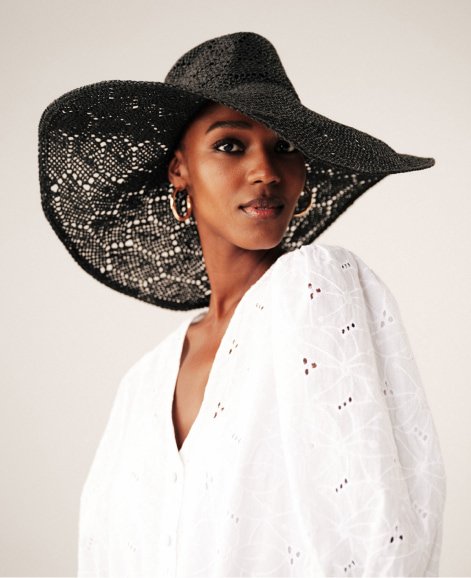 A woman wearing a white blouse and black summer hat.