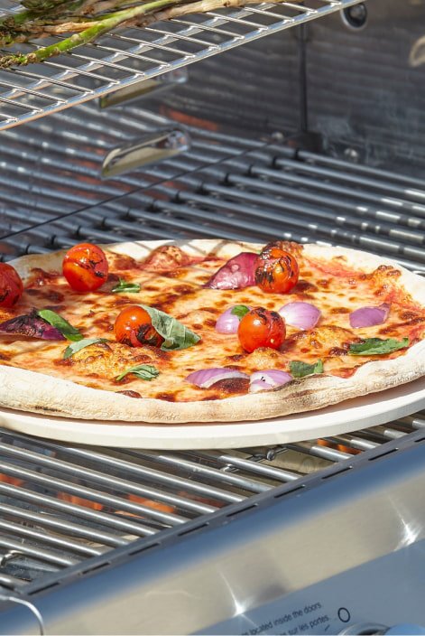 A pizza getting cooked on an outdoor grill.