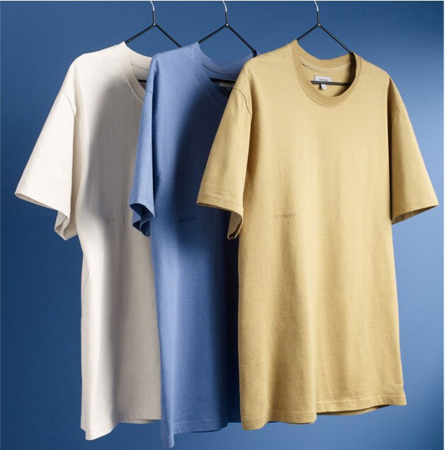 Three different coloured t-shirts on hangers in front of a blue background.