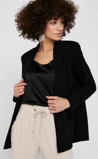 Woman wearing a black vest, blazer and beige trousers.