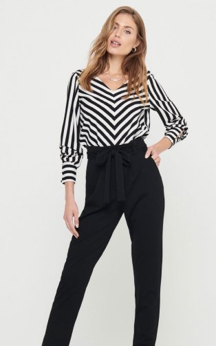 Woman wearing a black and white striped top and black trousers.