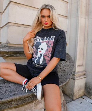 Woman poses sitting on step wearing grey Cruella de Vil t-shirt, black cycling shorts, red and white striped socks and navy lace-up pumps.