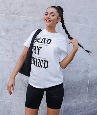 Woman poses smiling holding end of ponytail wearing white read my mind slogan t-shirt, black cycling shorts and black handbag.