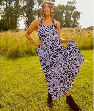 Woman poses holding the hem of monochrome animal print maxi dress with black lace-up boots.