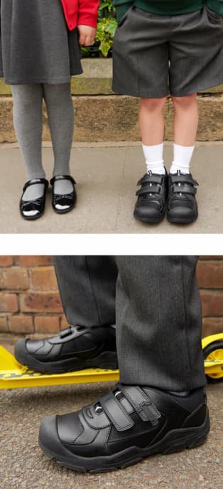 Legs of girl wearing grey skirt, grey tights and black patent 1 strap ballet shoes next to legs of boy wearing grey shorts, white socks and black 2 strap school shoes. Close up shot of boys feet wearing black 2 strap school shoes with one foot raised on yellow scooter.