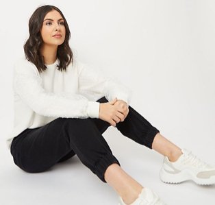 Woman wearing a white jumper with black joggers and white trainers.