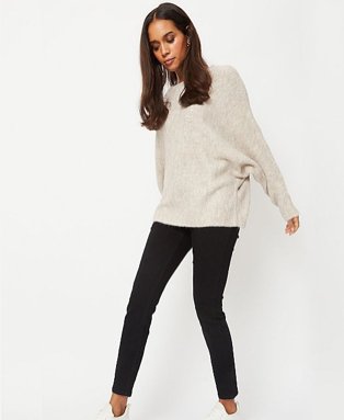 Woman wearing a beige jumper with black jeans and white trainers.