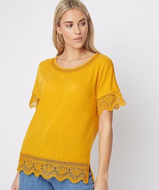 Woman wearing a mustard coloured t-shirt with lace trimmings and light blue jeans.