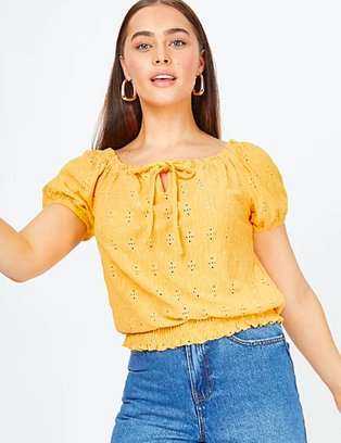 Woman poses wearing yellow open stitch cheese cloth t-shirt and mid wash blue denim shorts.
