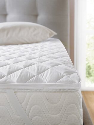 Double bed with grey quilted headboard, white mattress with mattress protector and pillow.