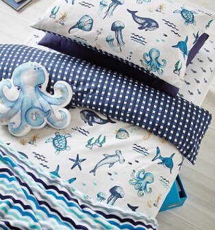 Layers of blue and white bedding printed with sea creatures and polka and stripey patterns with octopus cushion.
