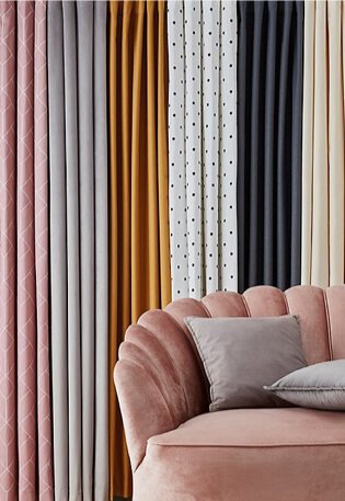 Pink, grey, mustard, white polka print and grey curtains hanging behind a pink pebble chair with grey scatter cushions. 