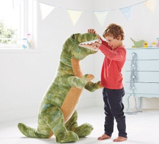 A boy in a red jumper and dark trousers in a playroom playing with a large plush T-Rex dinosaur toy.