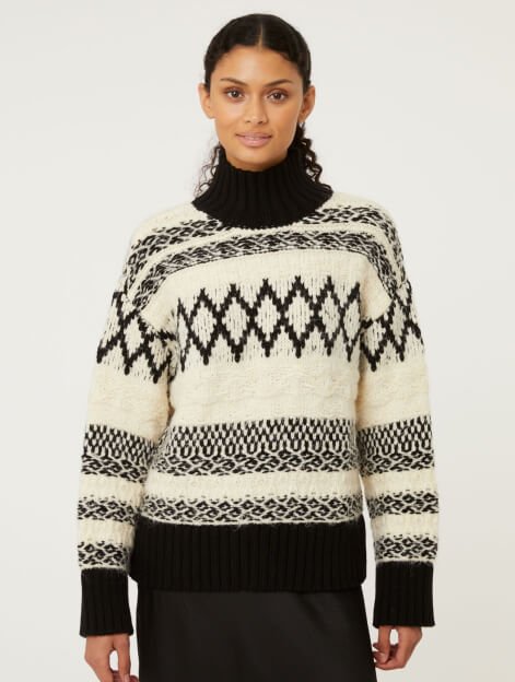 A woman wearing a cream and black chunky knitted funnel neck jumper.