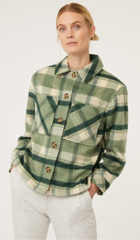 A woman wearing a green checked shacket and white trousers.