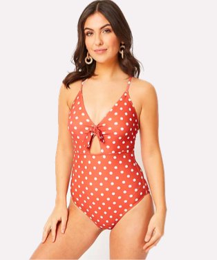 Woman poses wearing red and white polka dot cut out swimsuit.