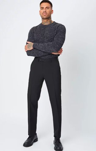 Man poses wearing black marl lightweight jumper tucked into black regular fit trousers and wide fit black leather lace-up oxford shoes.