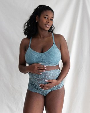 Woman poses with both hands on bump wearing maternity nursing blue lace comfort bra and maternity over bump blue lace knickers.
