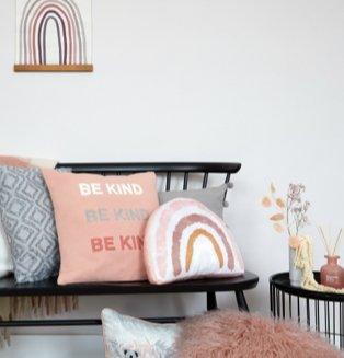 Black seat with rainbow cushion, slogan cushion and blue tile cushion next to matching black side table topped with artificial flowers and reed diffuser.