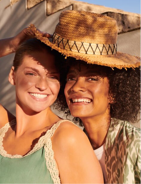 Two women wearing summer clothing and a summer hat.