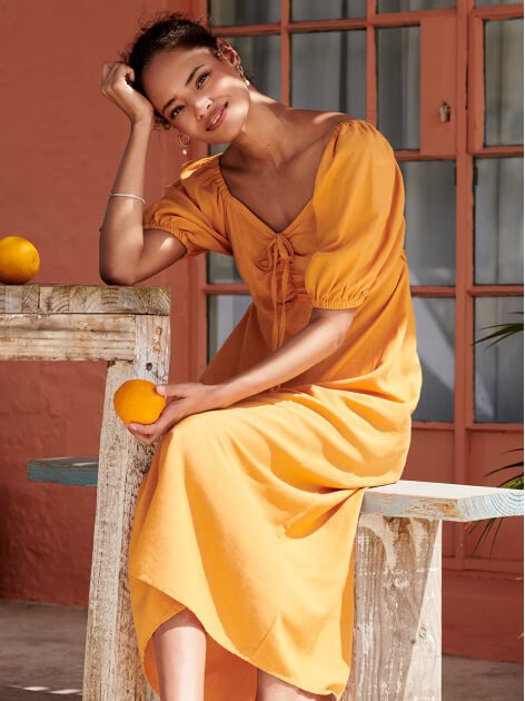 A woman sat at a table wearing an orange dress.
