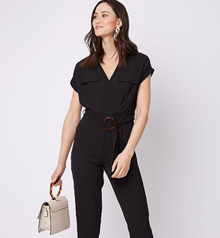 Woman wearing a black belted utility jumpsuit and holding a cream bag with a tortoiseshell handle