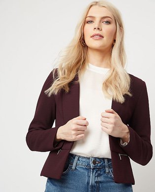 Woman in a burgundy blazer over a cream top and jeans