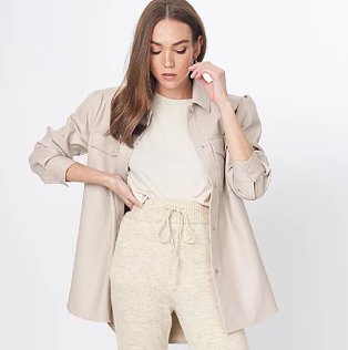 Brunette woman poses with hand on hip and hand raised to side of face wearing beige faux-leather longline shacket over white t-shirt and stone drawstring waistband joggers.