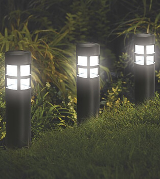 Three black lighthouse solar powered garden lights in a row in a garden