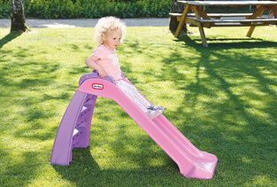 Girl going down a small pink slide in a garden